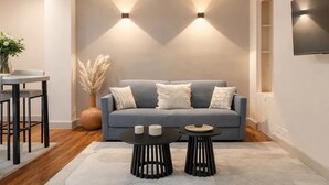 A living room with a grey sofa, two black side tables, a vase with pampas grass, and a flat-screen TV mounted on the wall. - 1525 Clef (Paris)