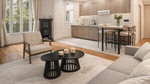 A modern living room with a sofa, a coffee table, and a fireplace. There is a kitchen area with wooden cabinets and a dining table. - 1525 Clef (Paris)
