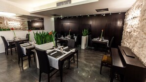 Een modern restaurant met donkerhouten tafels en stoelen, stenen muren en potplanten.