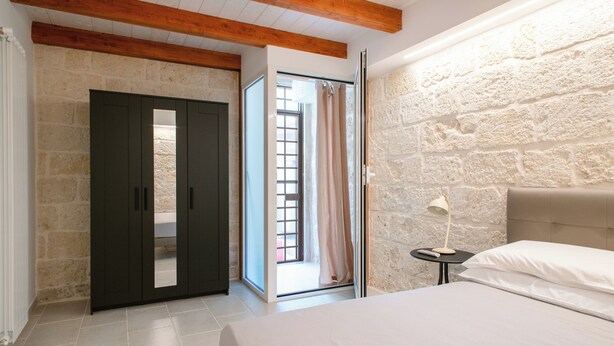 A bedroom with a bed, a wardrobe, a nightstand, and a stone wall. - [La Portulaca] Cozy Apt. in Molfetta (Molfetta)