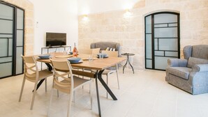 A dining area with a table, chairs, a television, and a stone wall. - [La Portulaca] Cozy Apt. in Molfetta (Molfetta)