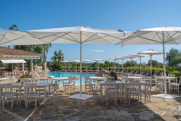 Un espace aménagé au bord de la piscine, avec des parasols blancs, des chaises longues et des tables.