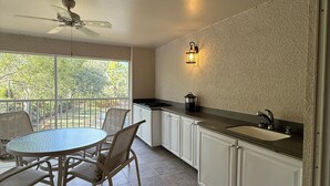 A kitchen with a dining table and chairs, a ceiling fan, a window with a view of trees, and a wall-mounted light fixture.