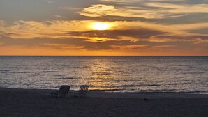 A beach with two sunlit chairs facing the ocean at sunset.