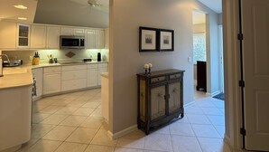 A modern kitchen with white cabinets, a microwave, and a dining area with a dark wooden cabinet.