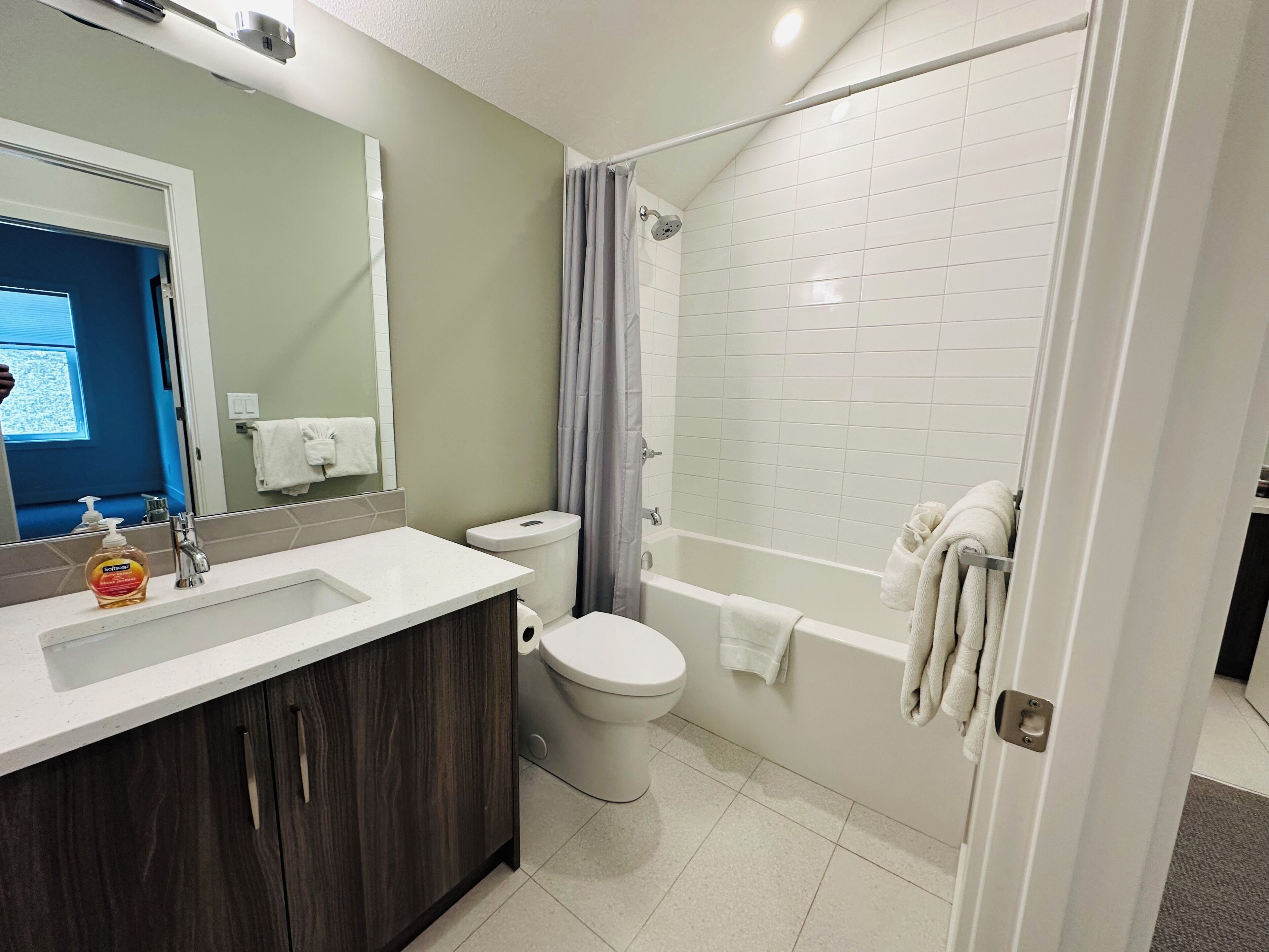 A modern bathroom with a white sink, dark wooden cabinet, white toilet, and a walk-in shower with a glass door.