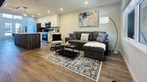 A modern living room with a sofa, coffee table, and a rug. There is a kitchen area with cabinets and appliances. - Skyridge Resort -Near Banff Entrance (Harvie Heights)
