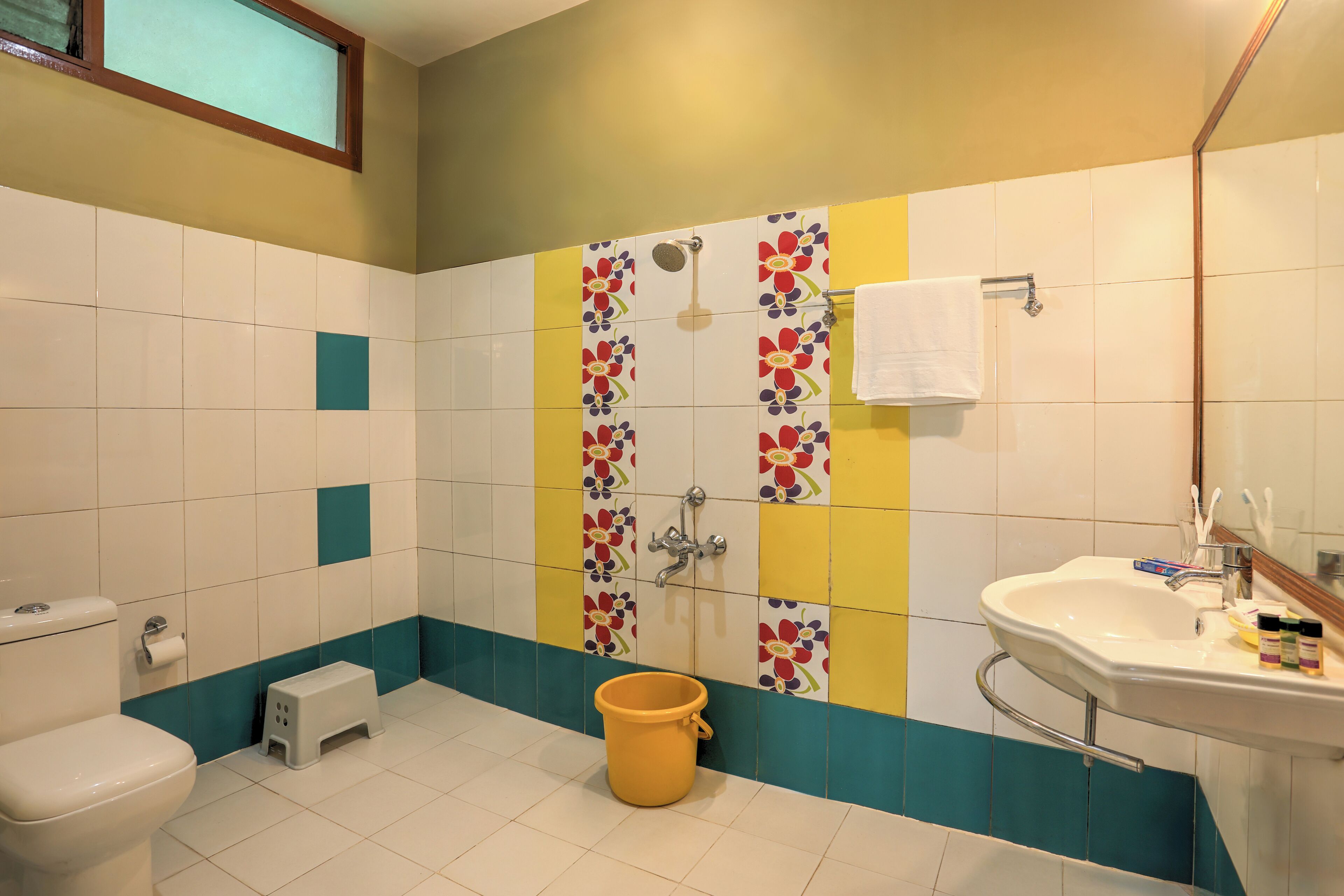 Baño con inodoro, lavamanos, ducha y un taburete.