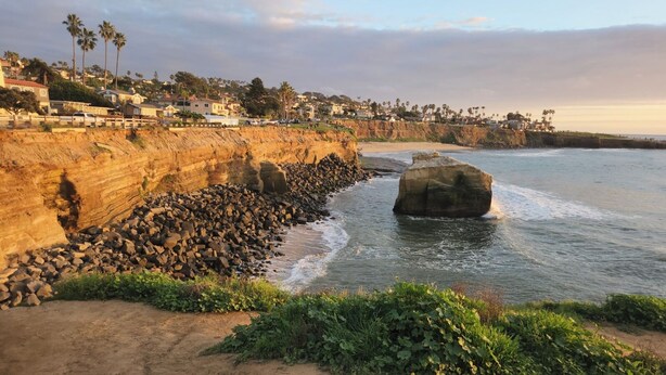 A coastal landscape with a rocky shoreline, a large boulder in the water, and a residential area in the background. - Stunning 4BR/3BA Home in Sunset Cliffs – Walk to Ocean (San Diego)