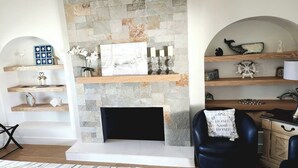 A living room with a stone fireplace, wooden shelves, and decorative items. - Stunning 4BR/3BA Home in Sunset Cliffs – Walk to Ocean (San Diego)