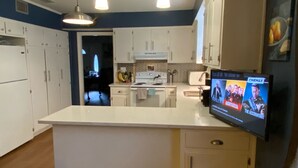 Una cucina moderna con mobili bianchi, un'isola centrale, un piano cottura e una televisione che mostra film.