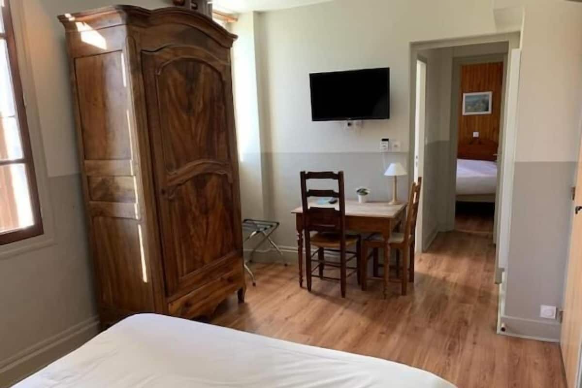 Een slaapkamer met een houten garderobe, een bed, een bureau met stoel, en een tv aan de muur.