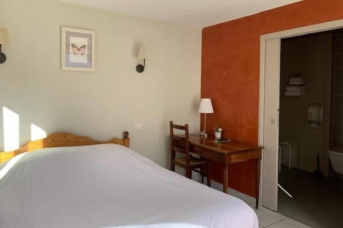 Hotelkamer met een bed, een bureau, een stoel, een lamp en een zichtbare badkamer door een geopende deur.