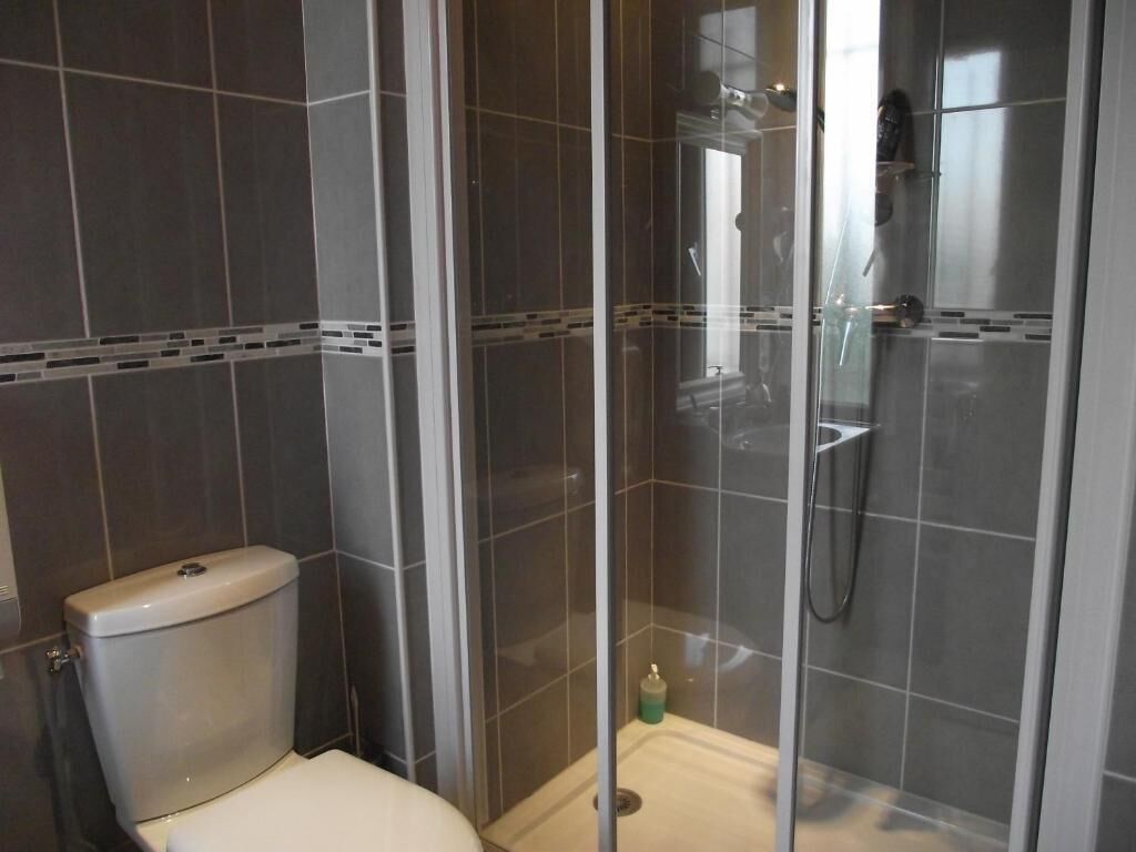 Un baño con inodoro, ducha con mampara de vidrio y paredes de azulejos.