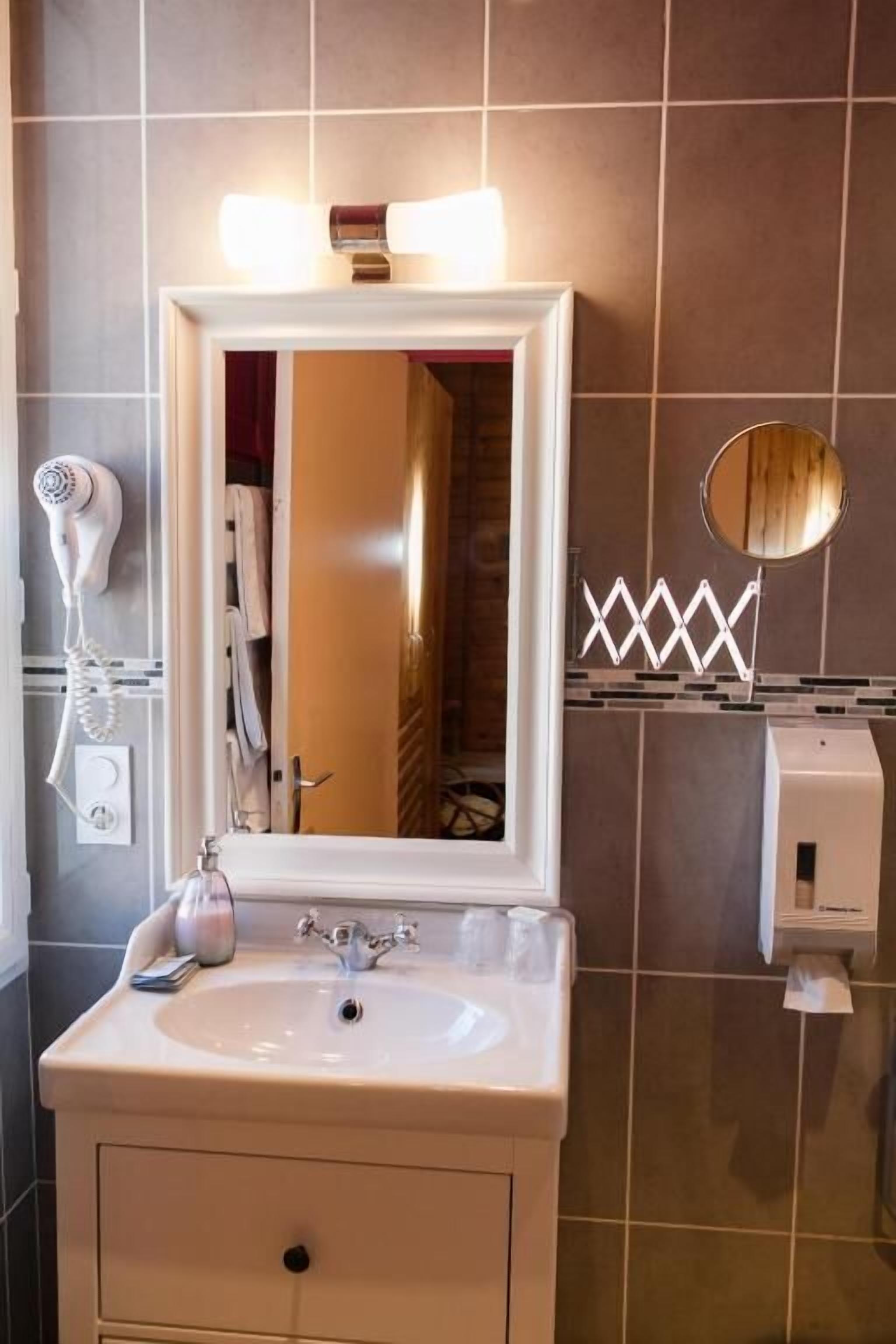 A bathroom with a white sink, a mirror with lights, a hairdryer, and a towel rack.