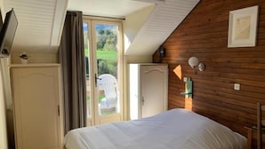 A bedroom with a bed, a wardrobe, a door, and a window with a view of greenery. - Au Sans Souci (Saint-Paul-lès-Monestier)