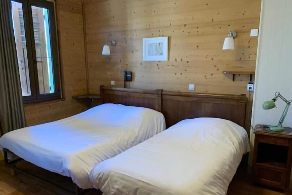 Een kamer met twee bedden, houten wanden, een raam en een nachtkastje met een lamp.