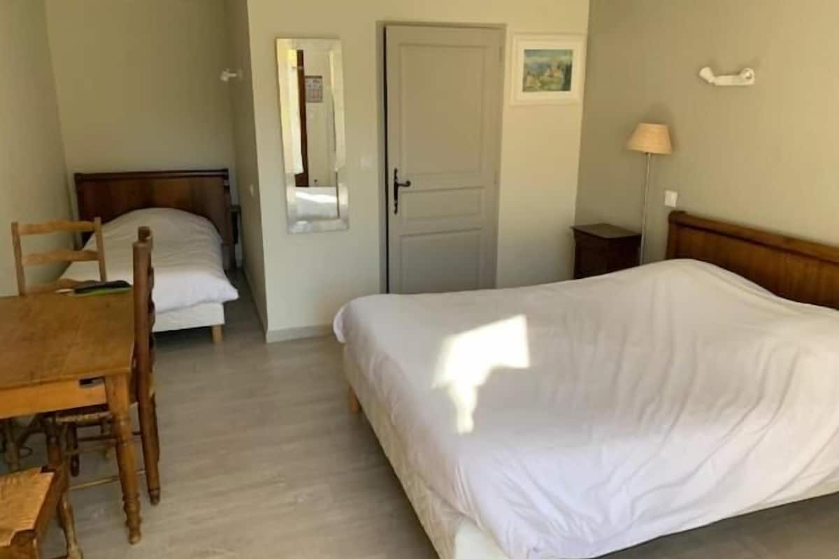 Een slaapkamer met een enkel bed, een houten stoel, een bureau, een spiegel en een deur.