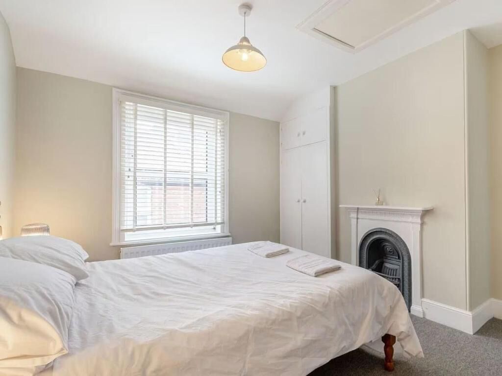 Een slaapkamer met een bed, een raam met zonwering, een open haard en een hanglamp.
