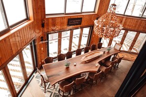 Een eetruimte met hoge plafonds, een grote houten tafel, meerdere stoelen en een hangende kroonluchter.