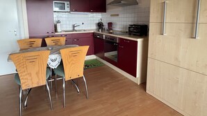 A compact kitchen with a microwave, toaster, and oven. There is a dining table with chairs and a small rug. - Northern Black Forest vacation app. 44 sqm, Dieter Hoffmann Freudenstadt-Kniebis. (Freudenstadt)
