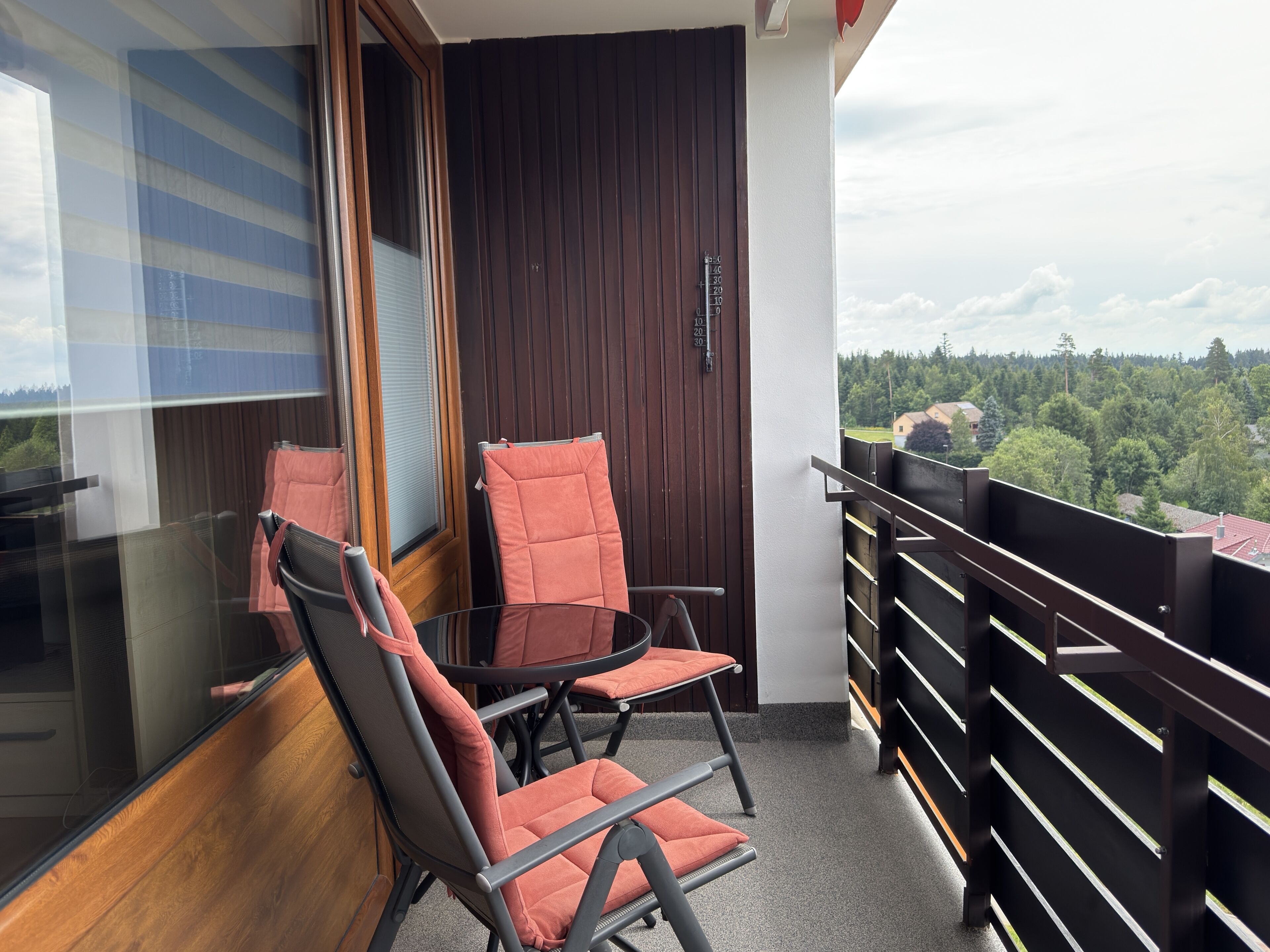 A balcony with two chairs, a table, and a view of a forested area.
