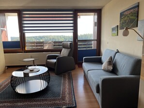 Een moderne woonkamer met een bank, fauteuils, een salontafel en uitzicht op een balkon met een balustrade.