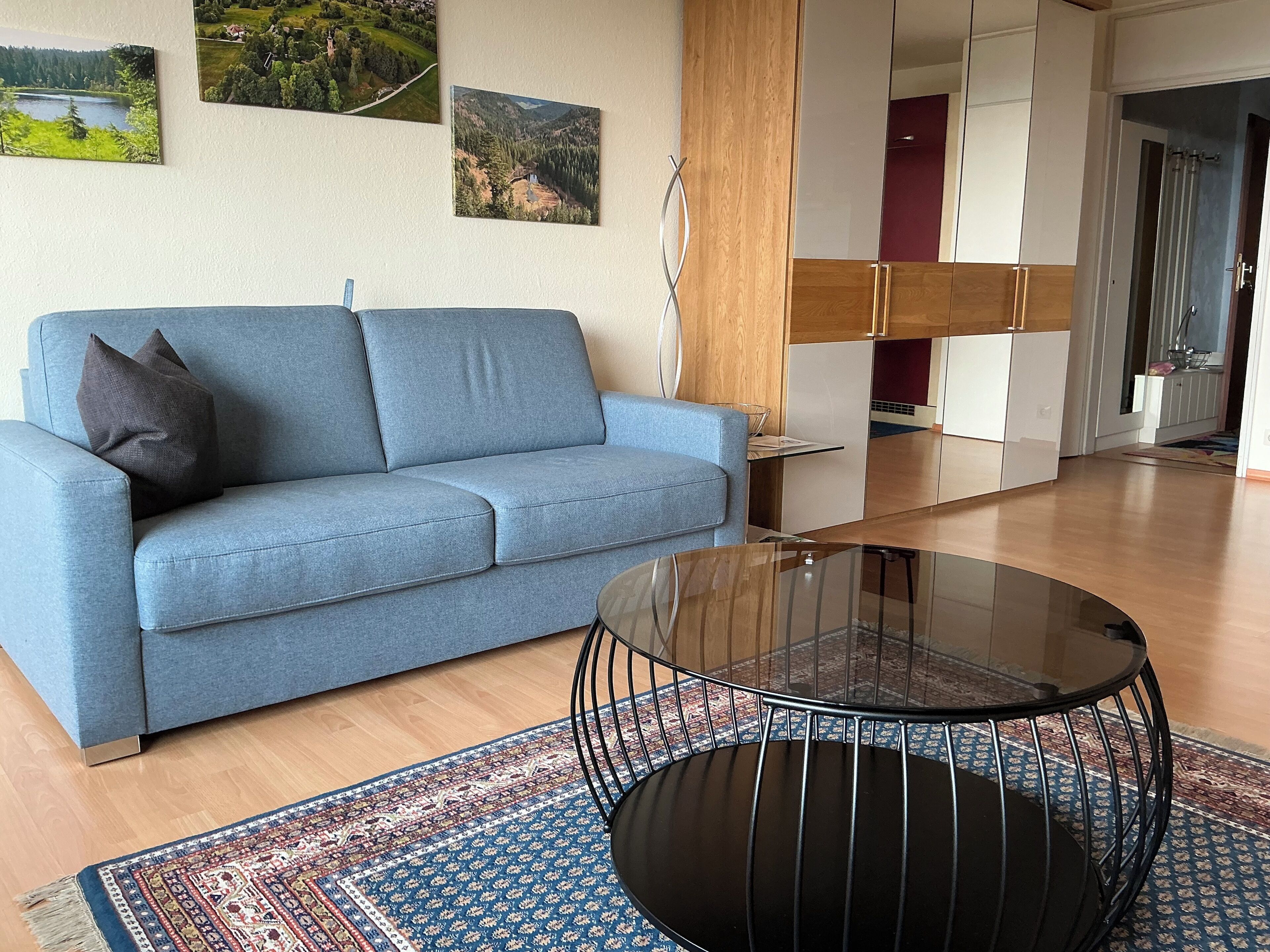 A modern living room with a sofa, a glass coffee table, and a patterned rug.
