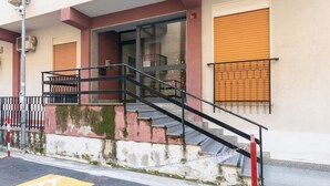 Un edificio con una escalera que lleva a una puerta, una ventana con contraventanas y una cerca de malla metálica.