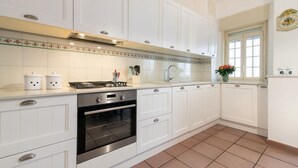 Una cocina con armarios blancos, estufa, horno y una ventana con flores.