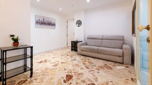 Una sala de estar con piso de piedra, un sofá, una mesita con una planta y un cuadro en la pared.