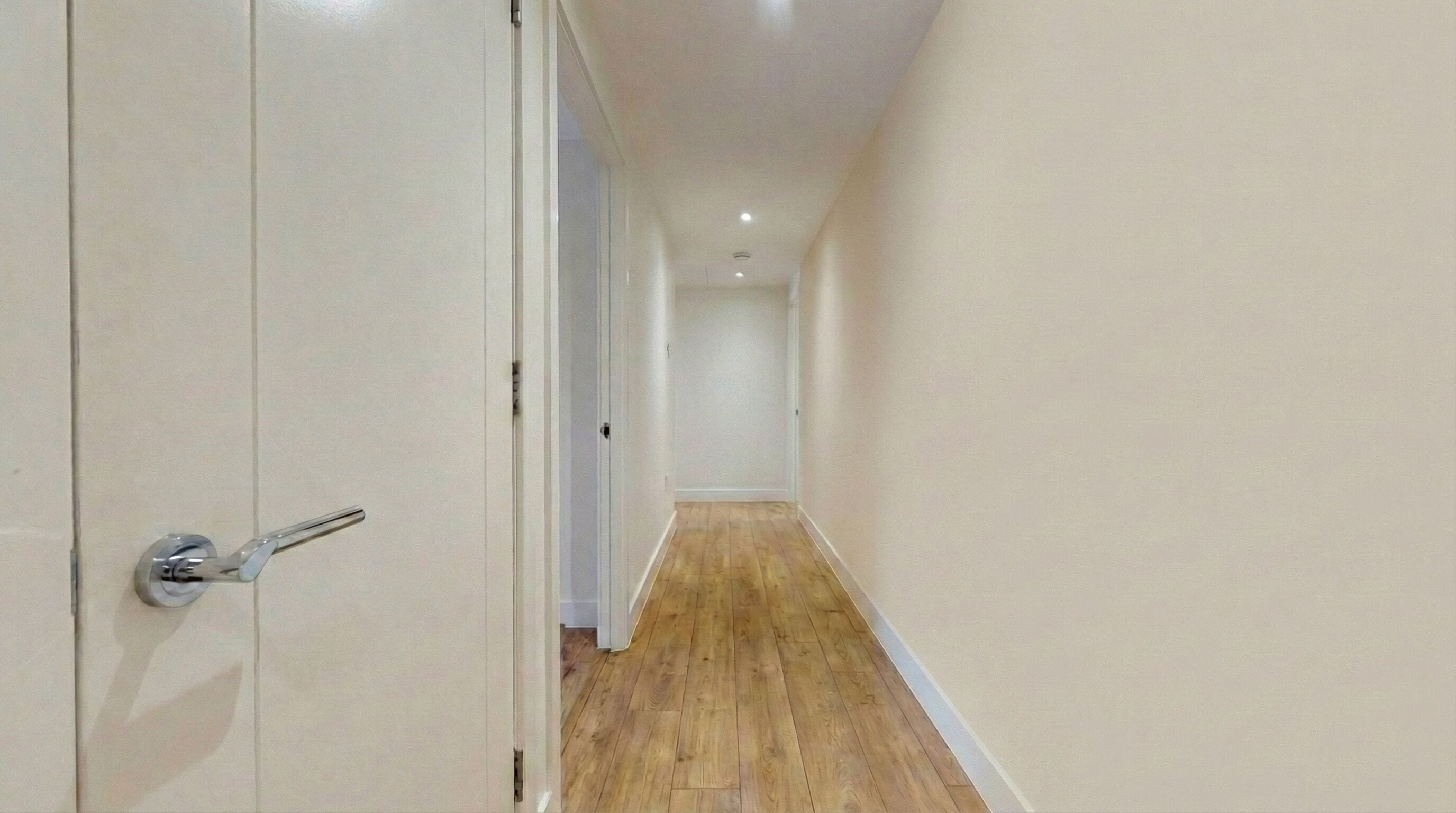 Un pasillo estrecho con suelo de madera y paredes blancas.