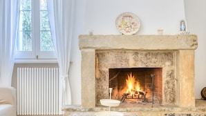 A cozy living room with a stone fireplace, a white radiator, and a window with white curtains. - Fantastic pool villa w/ private park 2km from sea (Castro)