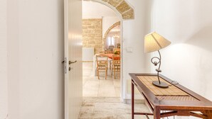 A hallway with a wooden table and lamp, leading to a dining area with a stone wall and a chandelier. - Fantastic pool villa w/ private park 2km from sea (Castro)