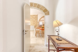 Un pasillo con una mesa de madera y una lámpara, que conduce a un área de comedor con una pared de piedra y un candelabro.