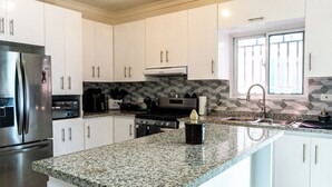 Cocina moderna con gabinetes blancos, encimera de granito, electrodomésticos de acero inoxidable y una ventana con rejas.