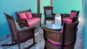 Un patio techado con mobiliario de mimbre y un ventilador de techo.