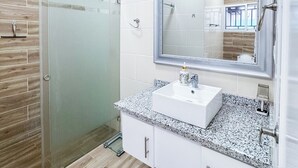 Et moderne badeværelse med en glasbrusekabine, en hvid vask med marmorbordplade og et stort spejl med dekorativ ramme.