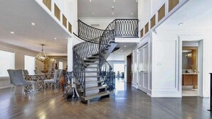 Un intérieur spacieux avec un escalier central en colimaçon, un plancher en bois et un coin repas doté de chaises modernes.