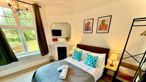 A hotel room with a bed, a mirror, a fireplace, and a window with curtains. - Boutique Double with Coastal Charm (Southwold)