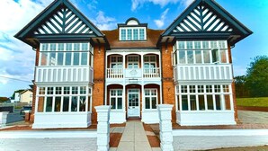 A two-story building with a symmetrical facade, featuring a central balcony with a sign, and a prominent entrance with a double door. - Boutique Double with Coastal Charm (Southwold)