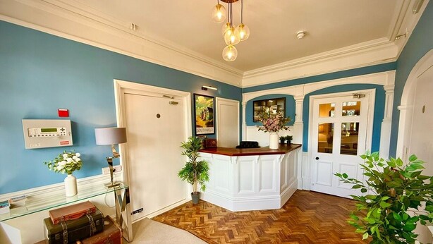 A reception area with a herringbone wooden floor, a reception desk, a plant, and a wall-mounted radio. - Boutique Double with Coastal Charm (Southwold)
