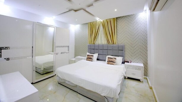 A modern bedroom with a large bed, a walk-in closet, and a herringbone-patterned wall. - iris life (Jeddah)
