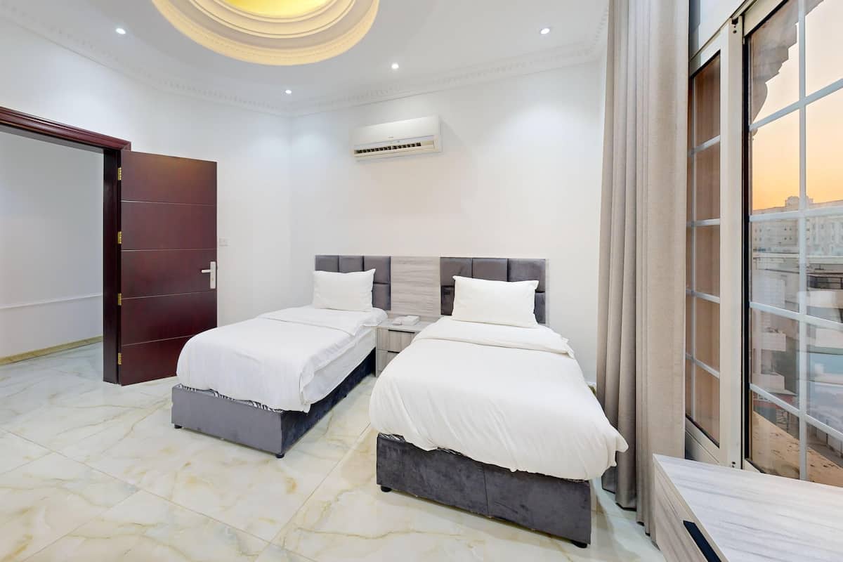 A hotel room with two beds, a large window, and an air conditioning unit.