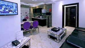 A modern living room with a TV, seating area, and a kitchen in the background. - iris life (Jeddah)