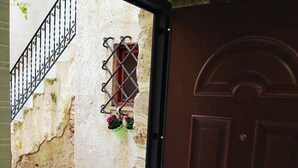 A brown door with a brass doorknob, a metal gate with a chain, and a brick wall with a window and hanging flower pots. - Newly renovated furnished studio apartment in the Center of funds LT (Fondi)