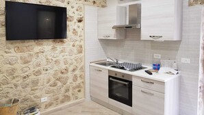 A modern kitchen with a stone wall, a flat-screen TV, white cabinetry, and an oven. - Newly renovated furnished studio apartment in the Center of funds LT (Fondi)