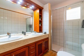 A bathroom with two sinks, a mirror, wooden cabinets, and a glass shower enclosure. - Villa Papagayo Faro by Villa Plus (Playa Blanca)