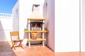 A small outdoor grill area with a chimney, a wooden chair, and a tiled floor. - Villa Papagayo Faro by Villa Plus (Playa Blanca)