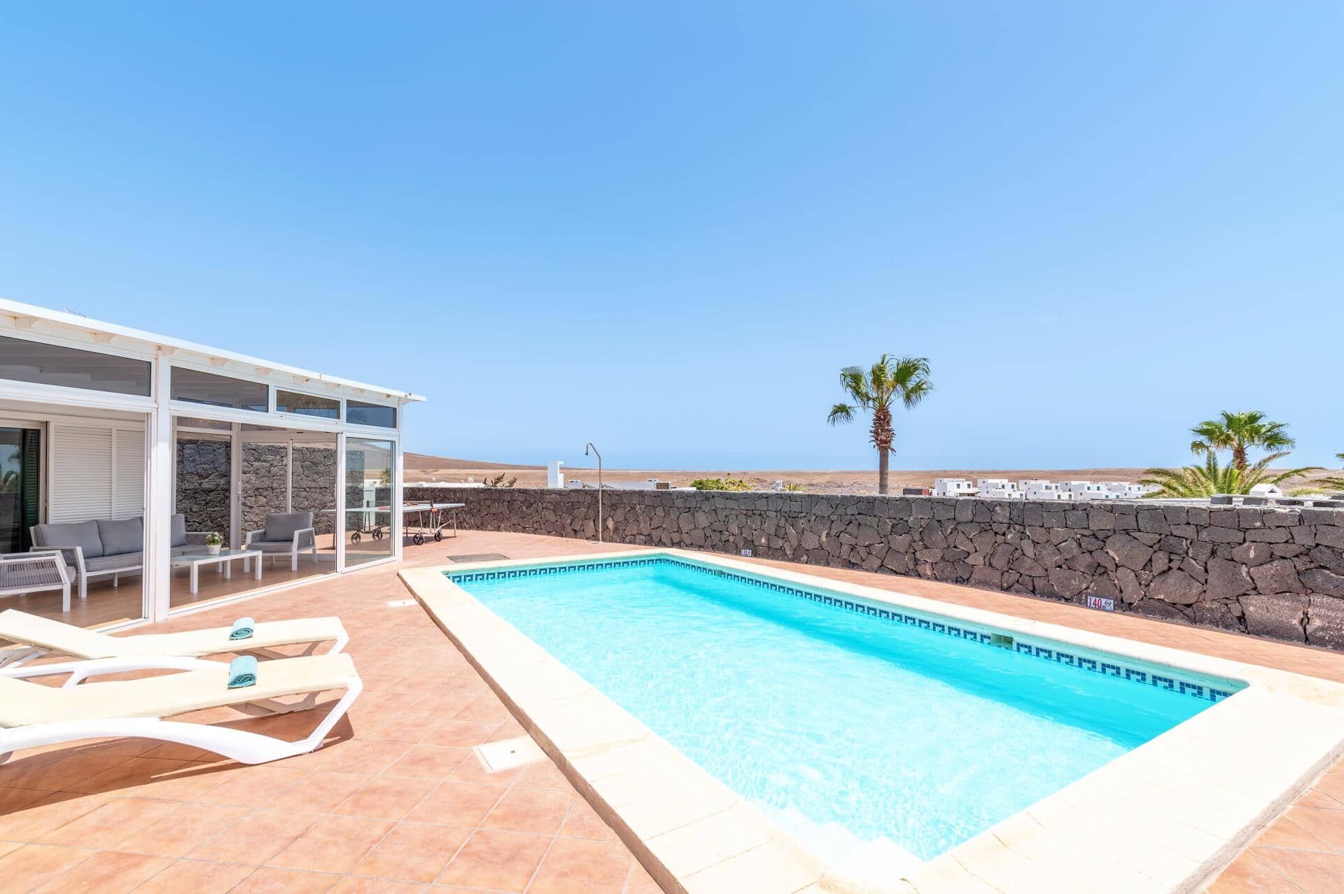 A pool area with lounge chairs, a covered seating area, and a stone wall.